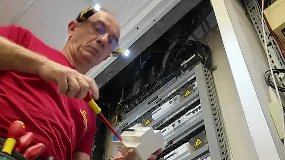 Électricien ERA Électricité équipé d'une lampe frontale LED, en intervention sur un tableau électrique à Genay